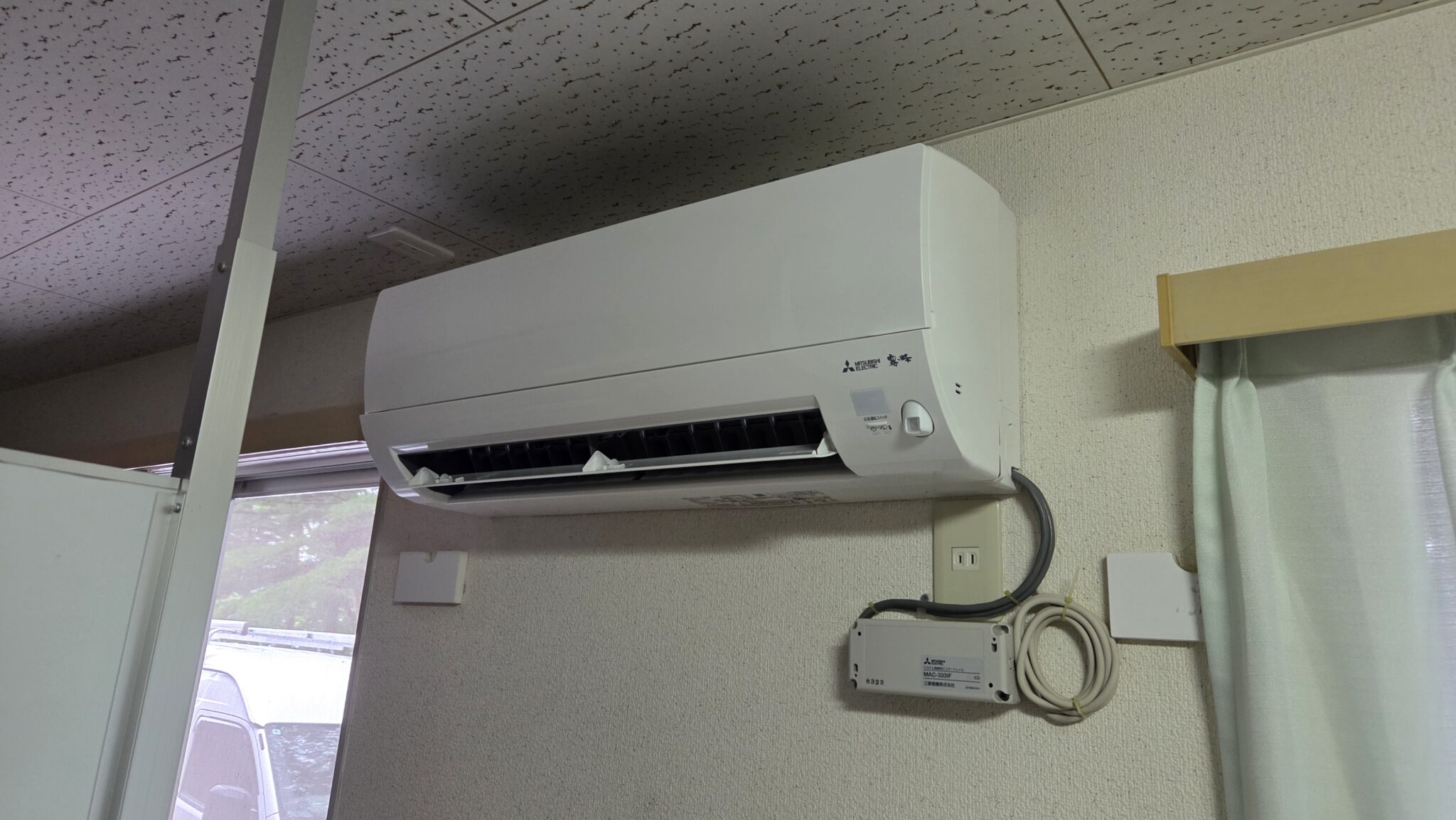 学生寮の居室に設置された三菱電機製の壁掛形室内機と、その下のインターフェース